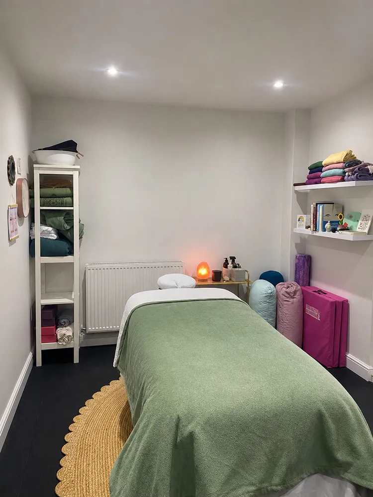 Zoe's treatment room, with a massage table made up with a green blanket on a woven rug