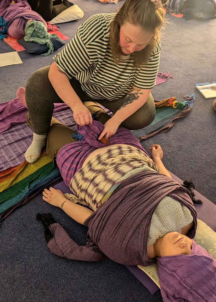 Zoe giving rebozo bodywork to a person lying on the floor wrapped in scarves