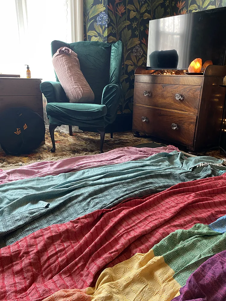 Colourful rebozo scarves spread across the floor in front of a green armchair