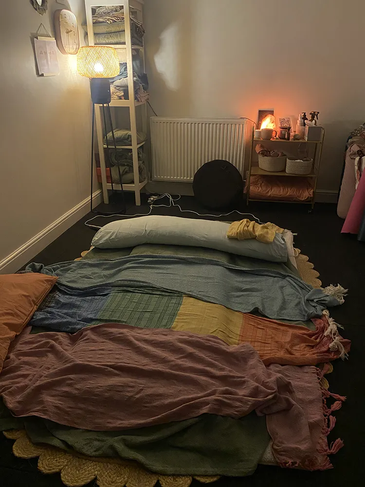Scarves, blankets and a bolster layered on a mattress in warm lamplight.