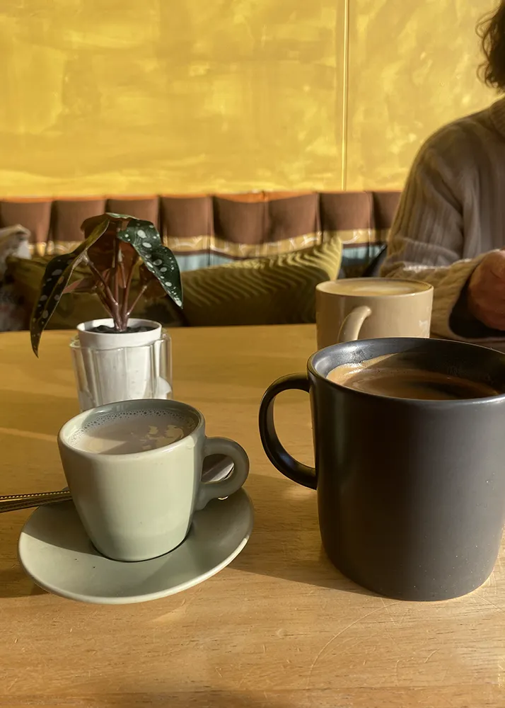 A cup of tea and a coffee on a wooden café table beside a small leafy plant