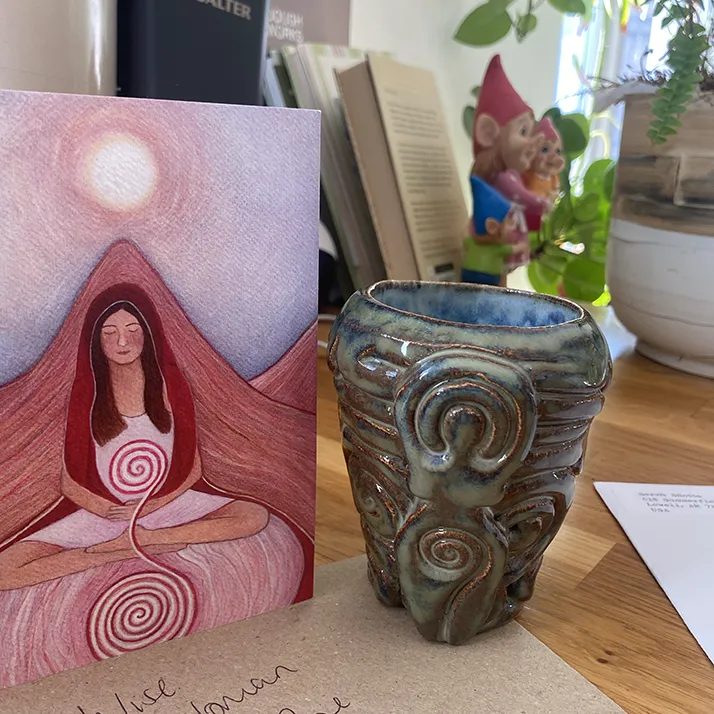 wise-woman A hand-made ceramic cup beside a painting of a seated woman with a spiral on her belly